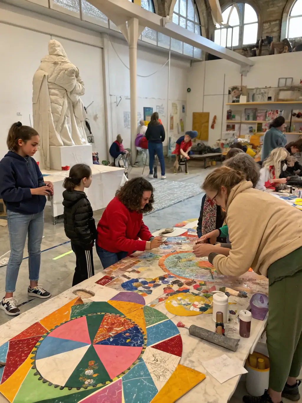 A lively scene of children and seniors participating together in a creative workshop, painting and crafting at large tables in a sunlit community hall.